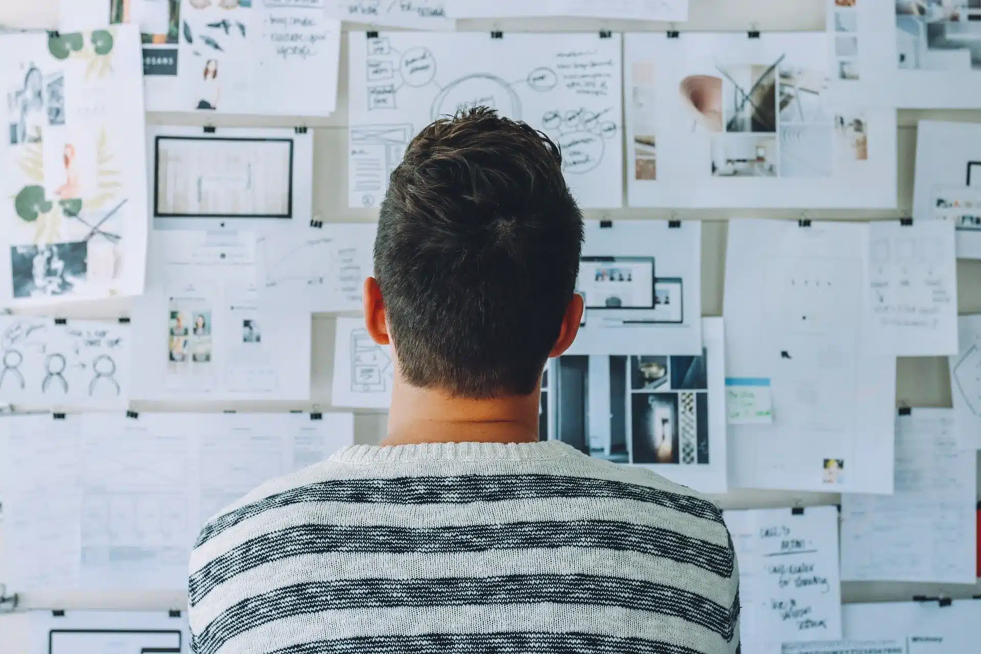shopware seo textbild shopware seo textbild. Das Bild zeigt eine Person, die vor einer Wand mit vielen Papierdokumenten und Notizen steht, die an der Wand befestigt sind.