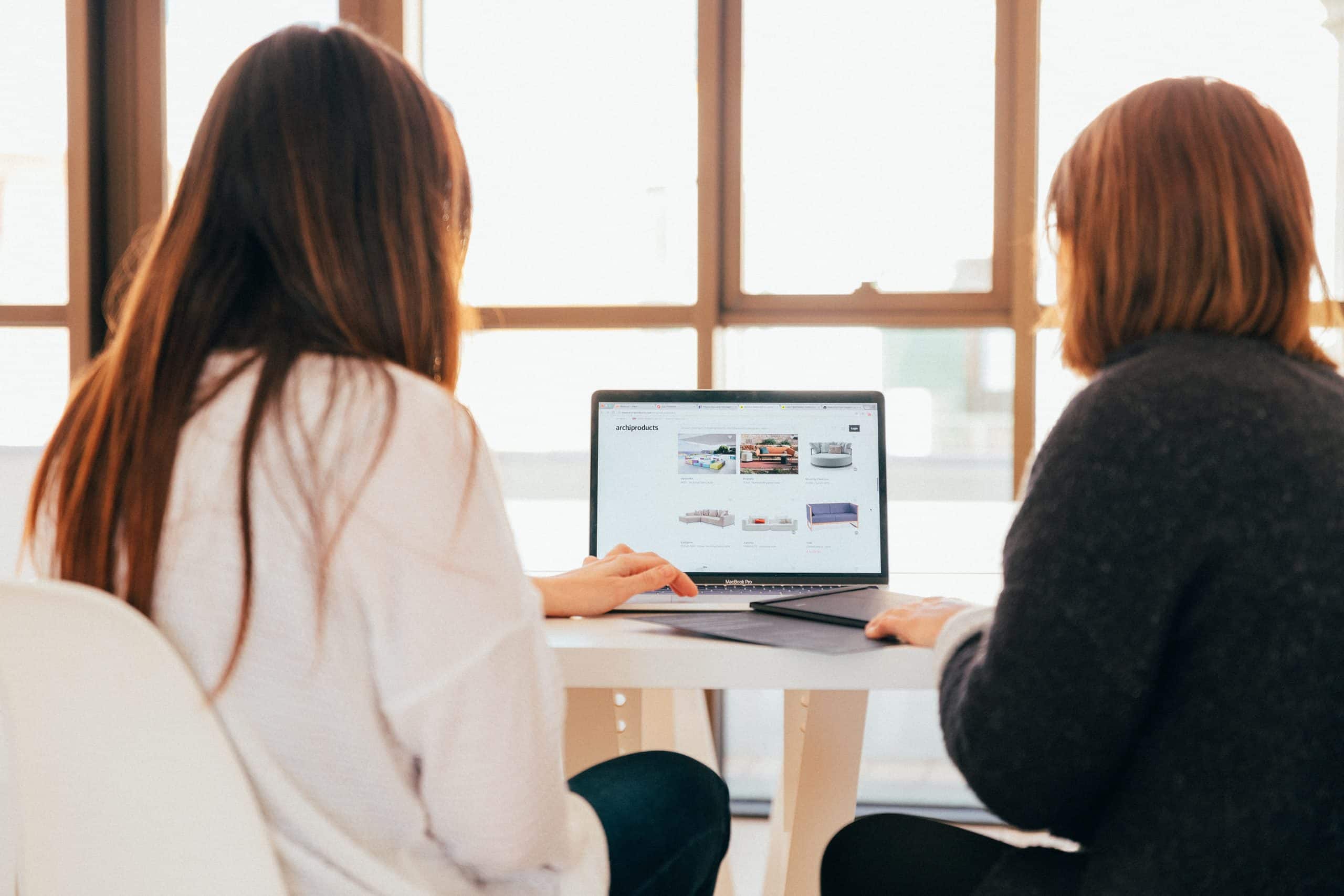 Marketing-Kolleginnen am Arbeiten Marketing-Kolleginnen sitzen nebeneinander und schauen auf einen Laptop